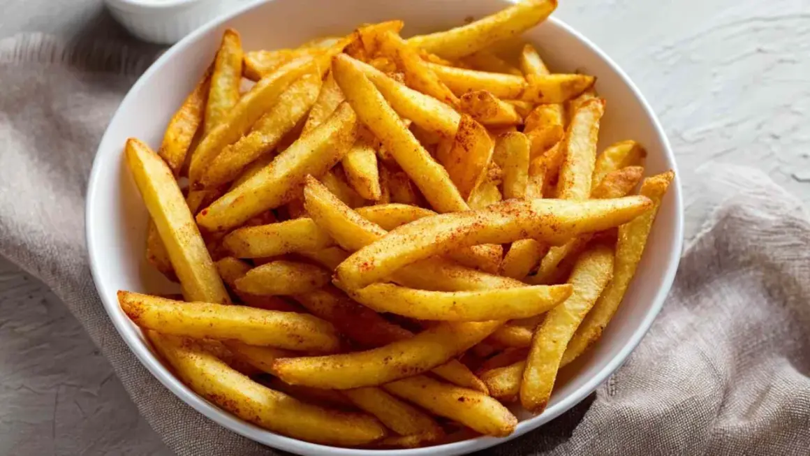 Chrupiące frytki z airfryer, posypane przyprawami, w białej misce. Idealna przekąska na każdą okazję.