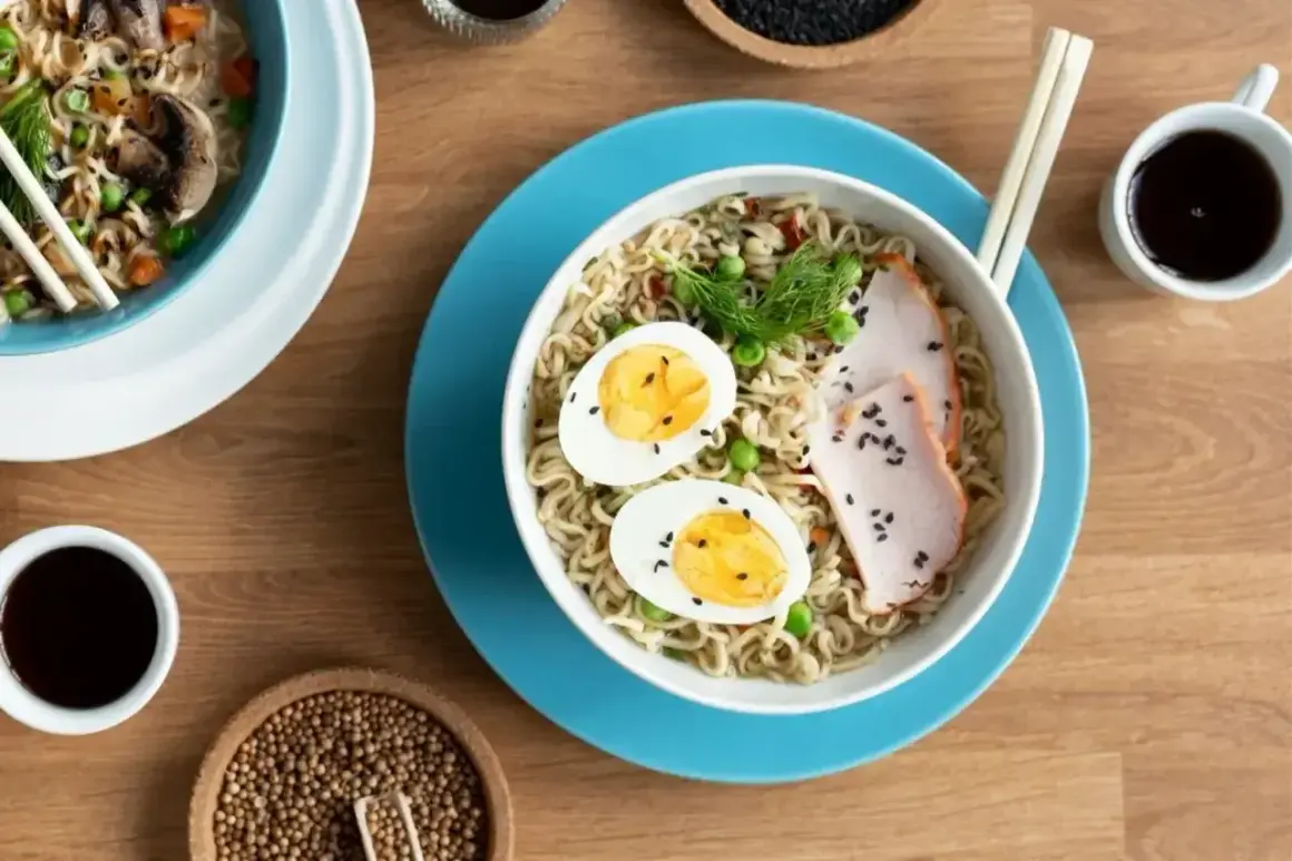 Miseczka z tantanmen, makaronem, jajkiem, mięsem i groszkiem. Obok sos sojowy i przyprawy.