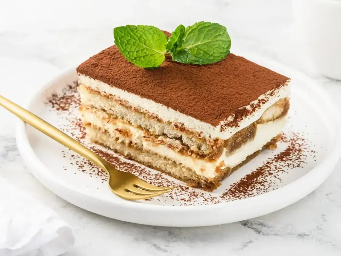 Pyszny kawałek tiramisu z mascarpone, posypany kakao i udekorowany miętą. Idealny sprawdzony przepis na deser.