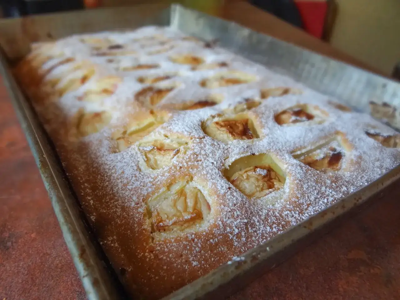 Szybkie i tanie ciasto na dużą blachę z jabłkami, posypane cukrem pudrem. Idealne na rodzinne spotkanie.