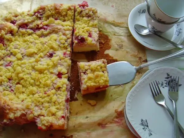 Pyszne ciasto drożdżowe z budyniem i owocami, posypane kruszonką. Gotowe do podania na talerzykach z widelcami.