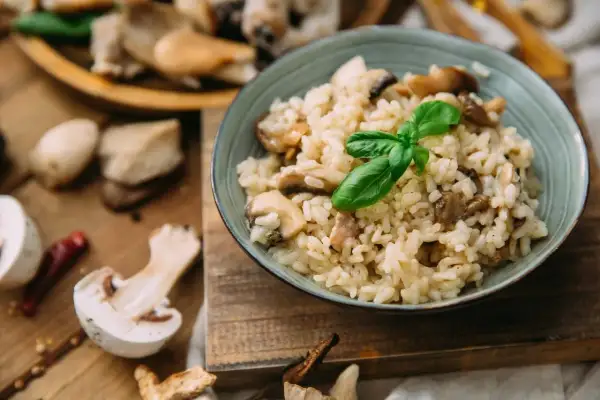 Aksamitny ryż do risotto z grzybami, udekorowany listkiem bazylii. Na drewnianej desce widać świeże grzyby i papryczkę chili.