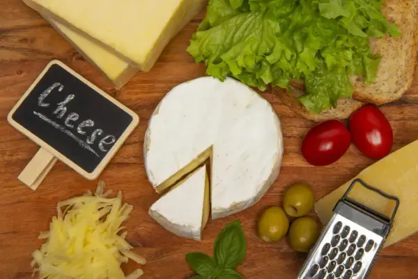 Deska serów: camembert, parmezan, żółty ser, oliwki, pomidorki, sałata i pieczywo. Ser corregio w centrum uwagi.