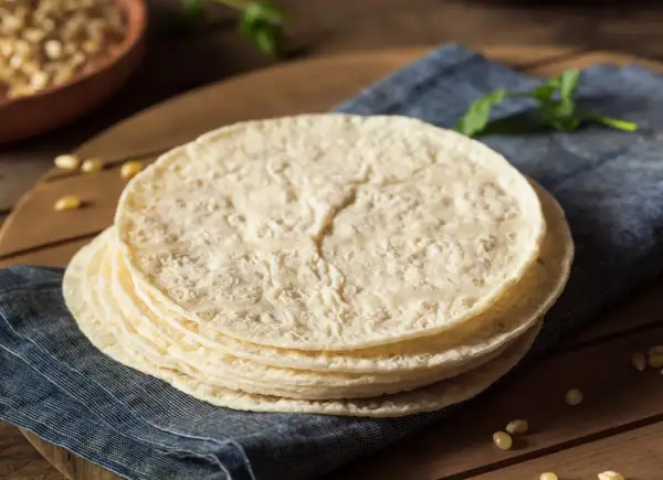 Stos świeżo upieczonych placków tortilla, które wyglądają jak z oryginalny przepis, leży na niebieskiej serwetce.