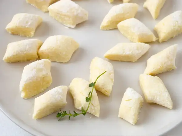 Kopytka z przepisu babci, delikatne i puszyste, posypane mąką, leżą na talerzu.