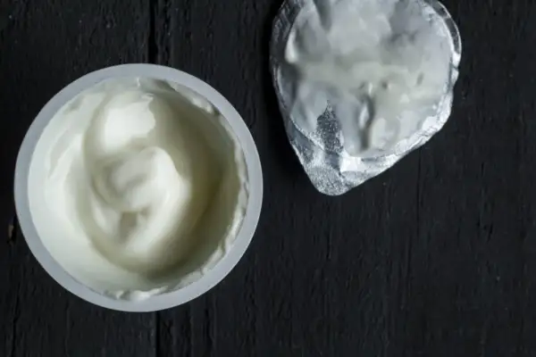 Gęsty, biały jogurt w kubeczku, obok srebrna folia. To skyr, islandzki przysmak bogaty w białko.