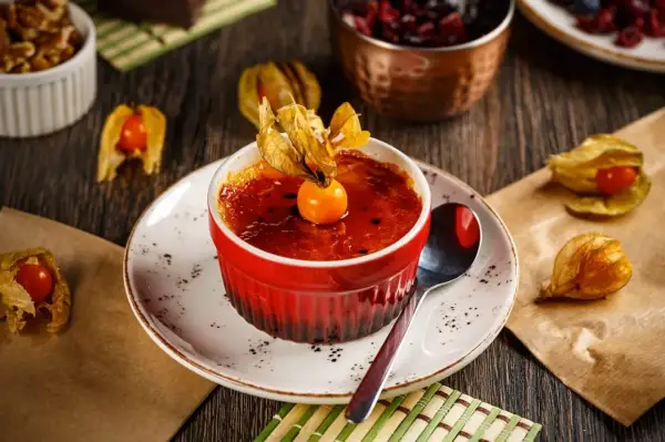 Słodka, karmelizowana crème brûlée w czerwonej kokilce, ozdobiona owocem miechunki.