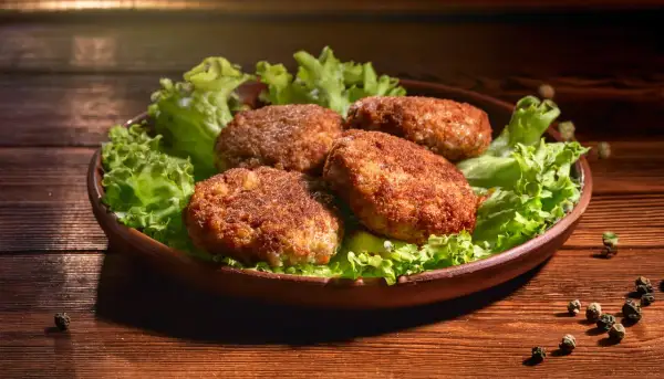 Cztery apetyczne kotlety mielone, idealnie wysmażone w airfryer, podane na liściach sałaty.