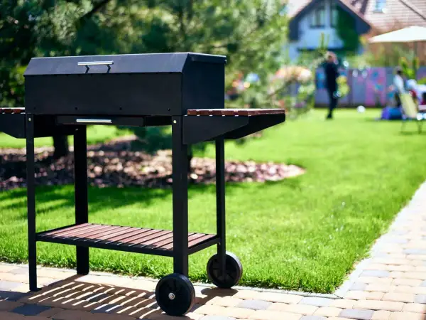 Czarny grill na kółkach w ogrodzie, gotowy na przyjęcie gości. Idealny pomysł na to, co na grilla tanio i smacznie.