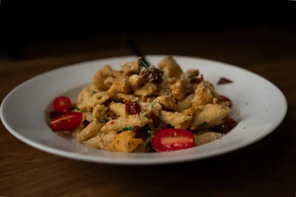 Penne z kurczakiem, suszonymi pomidorami i parmezanem, podane z pomidorkami koktajlowymi. Kremowy sos na bazie serka typu Philadelphia idealnie otula makaron.