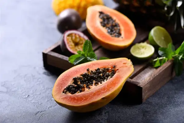 Dwa połówki papai z czarnymi nasionami, obok marakuja, limonki i mięta w drewnianej skrzynce.