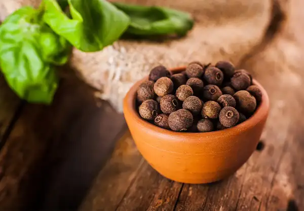 Garnek pełen aromatycznego ziela angielskiego na drewnianym blacie, obok zielone liście.